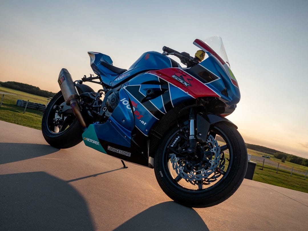 Blue Suzuki GSX-R sportbike with racing decals parked on a sunlit track under a warm golden sunset sky.