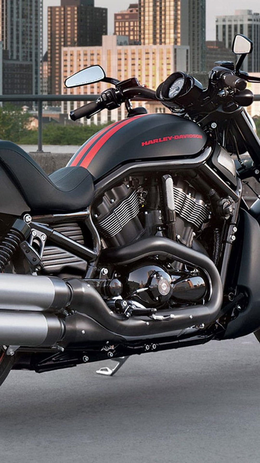 Harley-Davidson V-Rod motorcycle with red stripes and chrome exhaust parked before a blurred urban skyline.