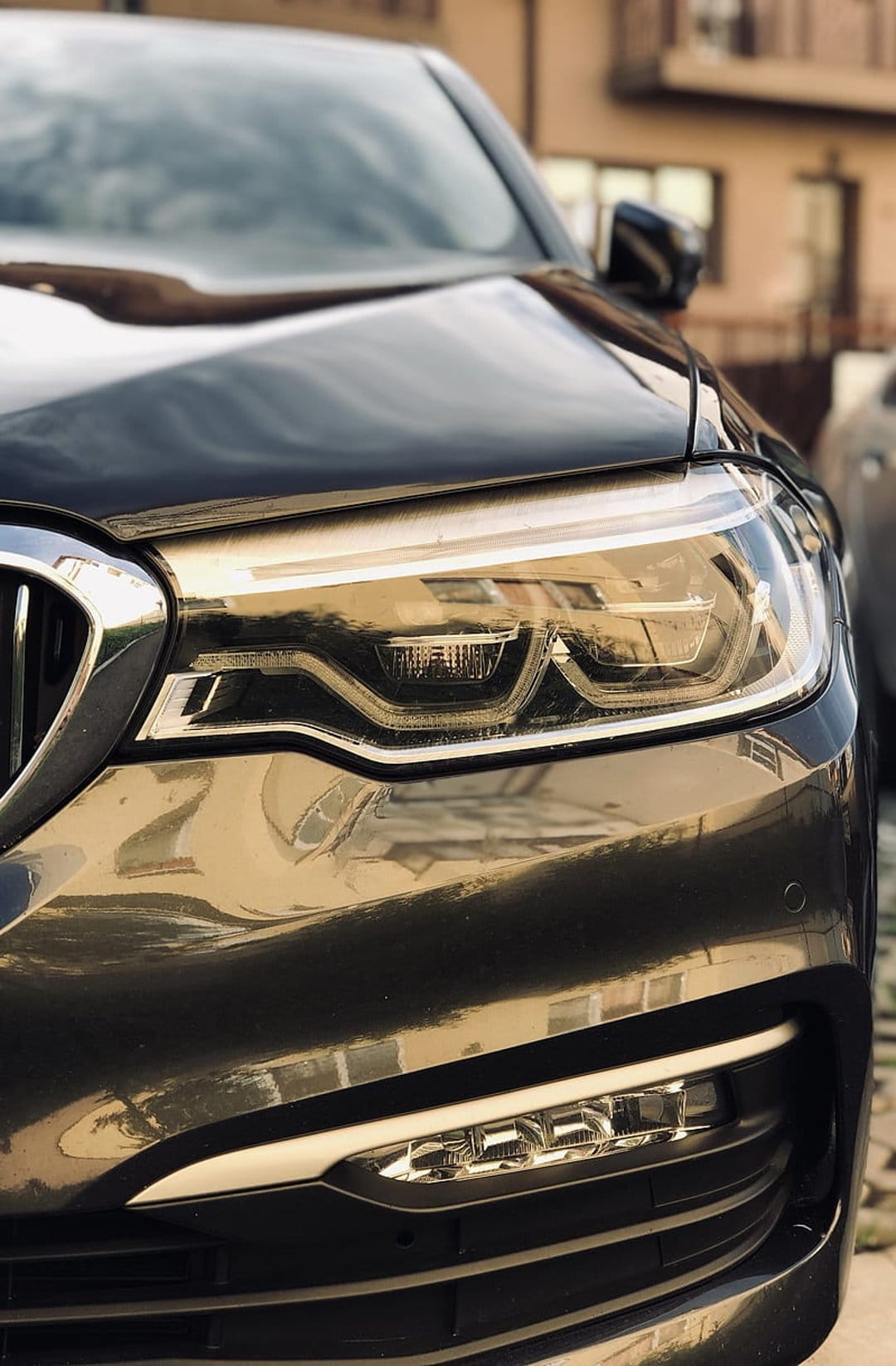 Black luxury car headlight with intricate LED optics and chrome housing reflected on polished dark paint.