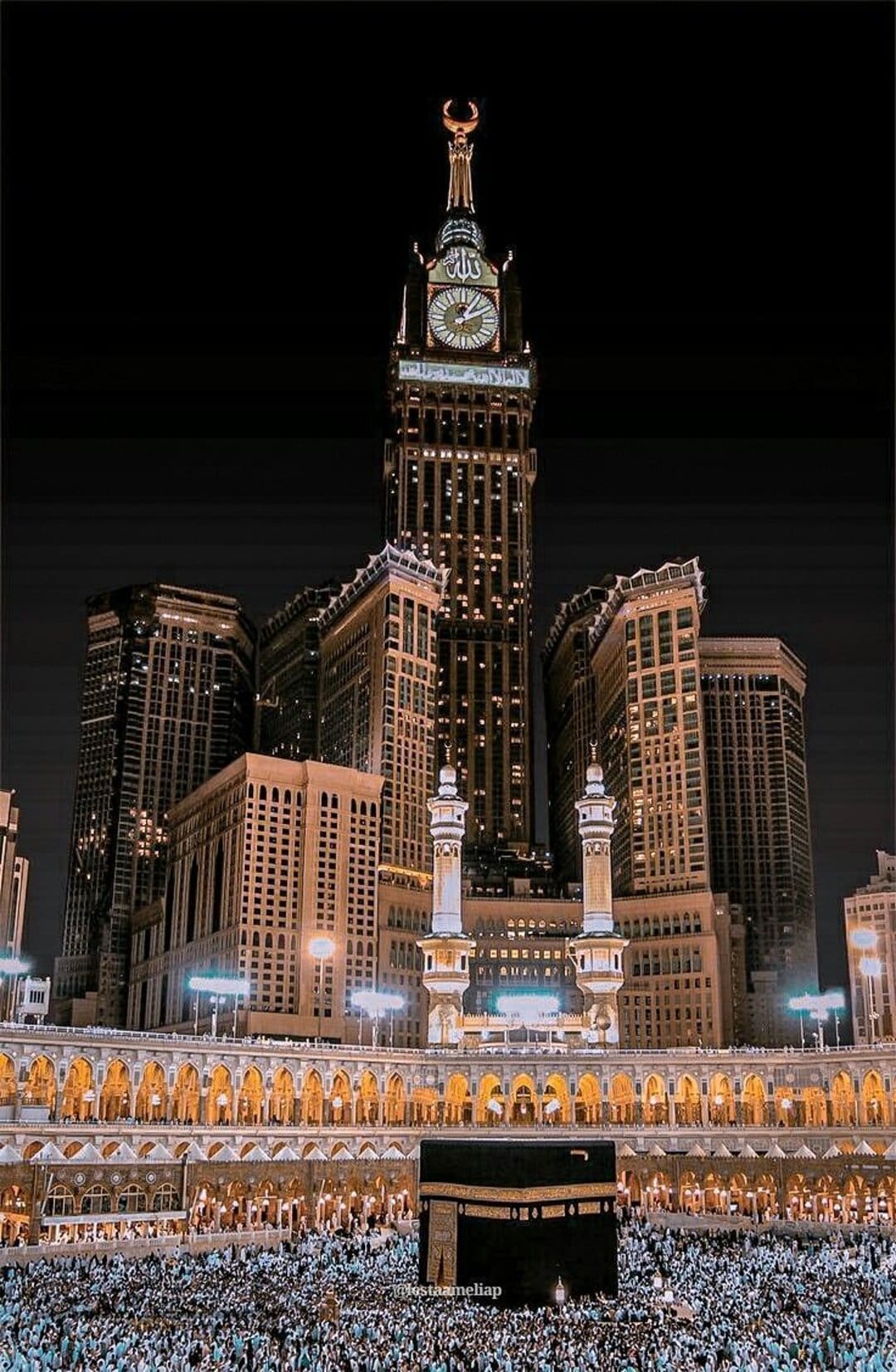 Abraj Al-Bait clock tower illuminates the night sky above the Kaaba and crowds in the Great Mosque courtyard.