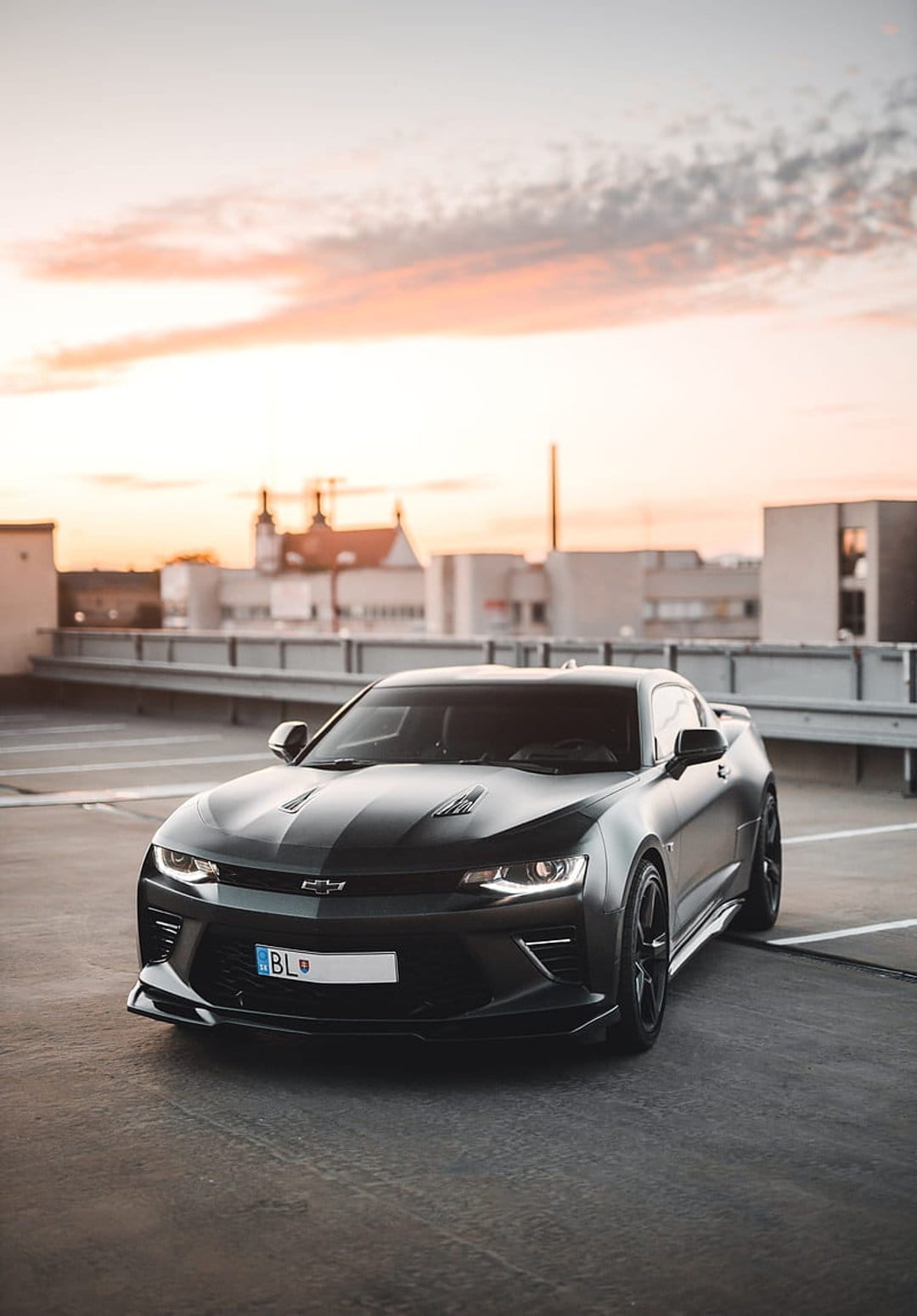 Black Chevrolet Camaro parked on a rooftop during sunset with warm orange light reflecting on its glossy paint.