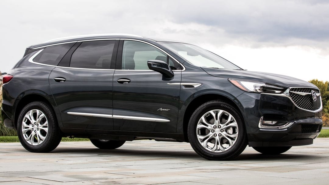 Dark grey Buick Enclave Avenir SUV side profile on stone pavement with chrome accents and overcast sky.
