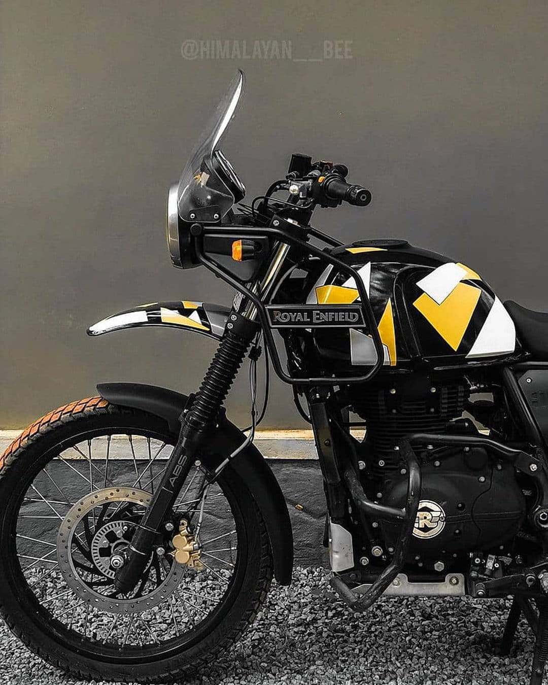 Royal Enfield Himalayan motorcycle with yellow geometric fuel tank decals, crash guards, and spoked wheels.