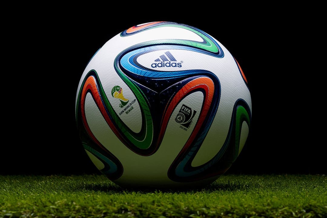 Adidas Brazuca soccer ball with colorful swirl patterns sits on green grass under soft studio lighting.