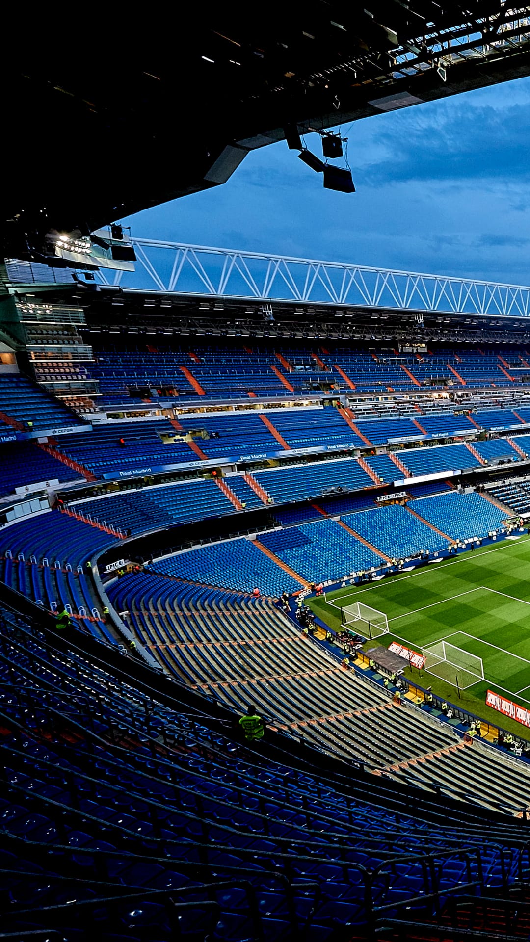 Santiago Bernabéu Stadium blue seats and green turf seen from above during twilight with bright floodlights.