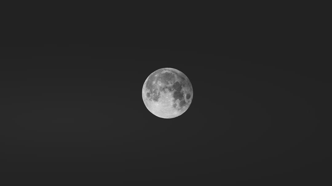 Full moon showing detailed craters and grey lunar plains against a pitch-black, starless night sky background.