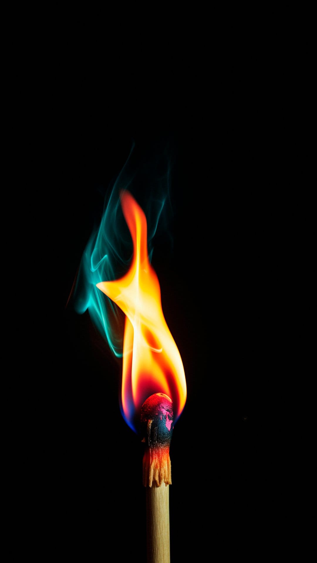 Wooden matchstick head erupting in bright orange fire and turquoise smoke against a dark black background.