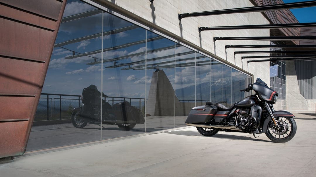 Black Harley-Davidson CVO Street Glide motorcycle reflecting in a large glass window of a modern building.