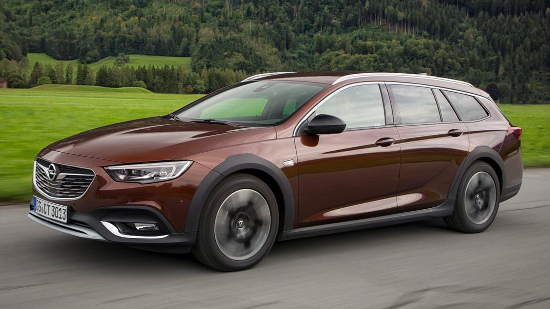 Brown Opel Insignia Country Tourer driving on a mountain road with blurred wheels and green forest background.