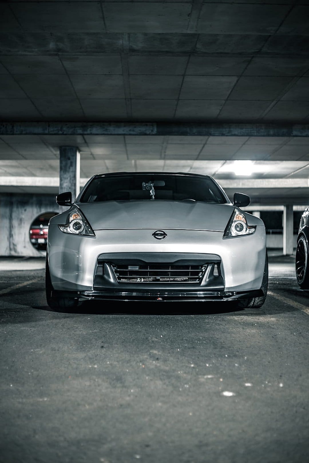 Silver Nissan 370Z sports car parked in a concrete garage with industrial lighting and aggressive front grille.
