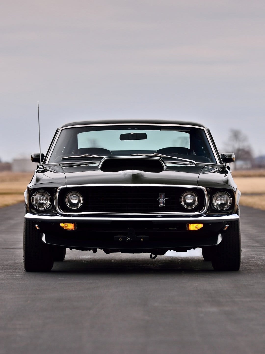 Front view of a black 1969 Ford Mustang with quad headlights and chrome bumper on an open asphalt road.