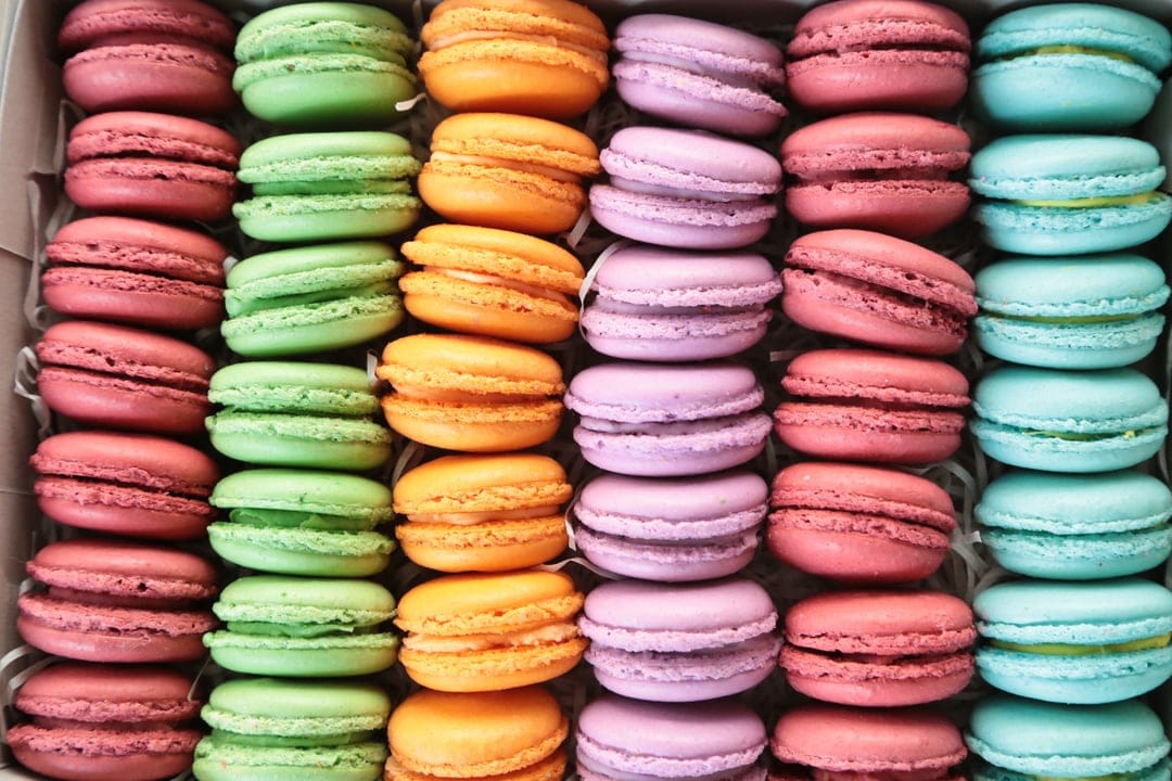 Pastel French macarons organized in neat rows inside a white box viewed from a top-down perspective.