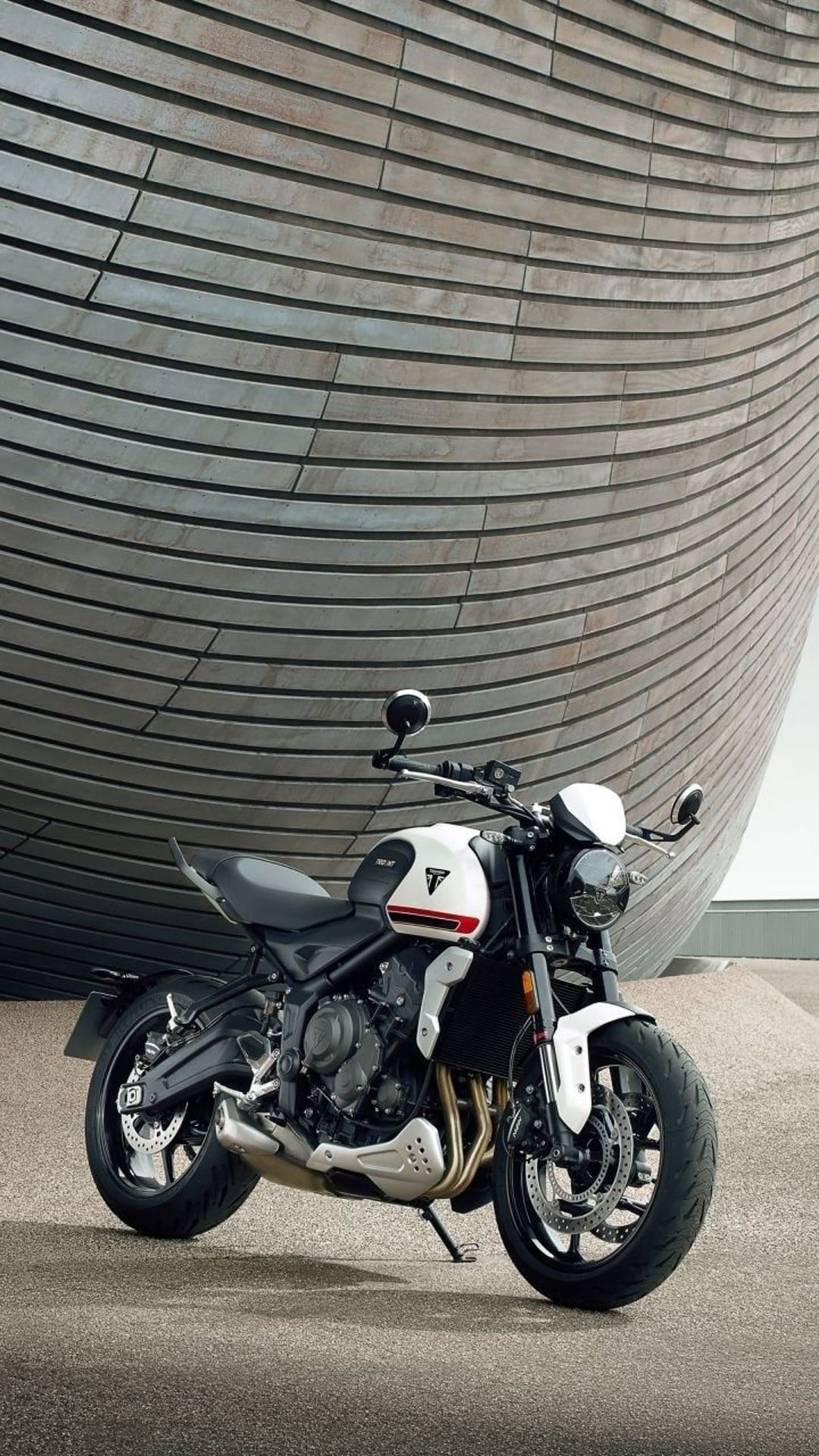 Triumph Trident motorcycle parked on concrete by a silver building with curved horizontal metal siding.