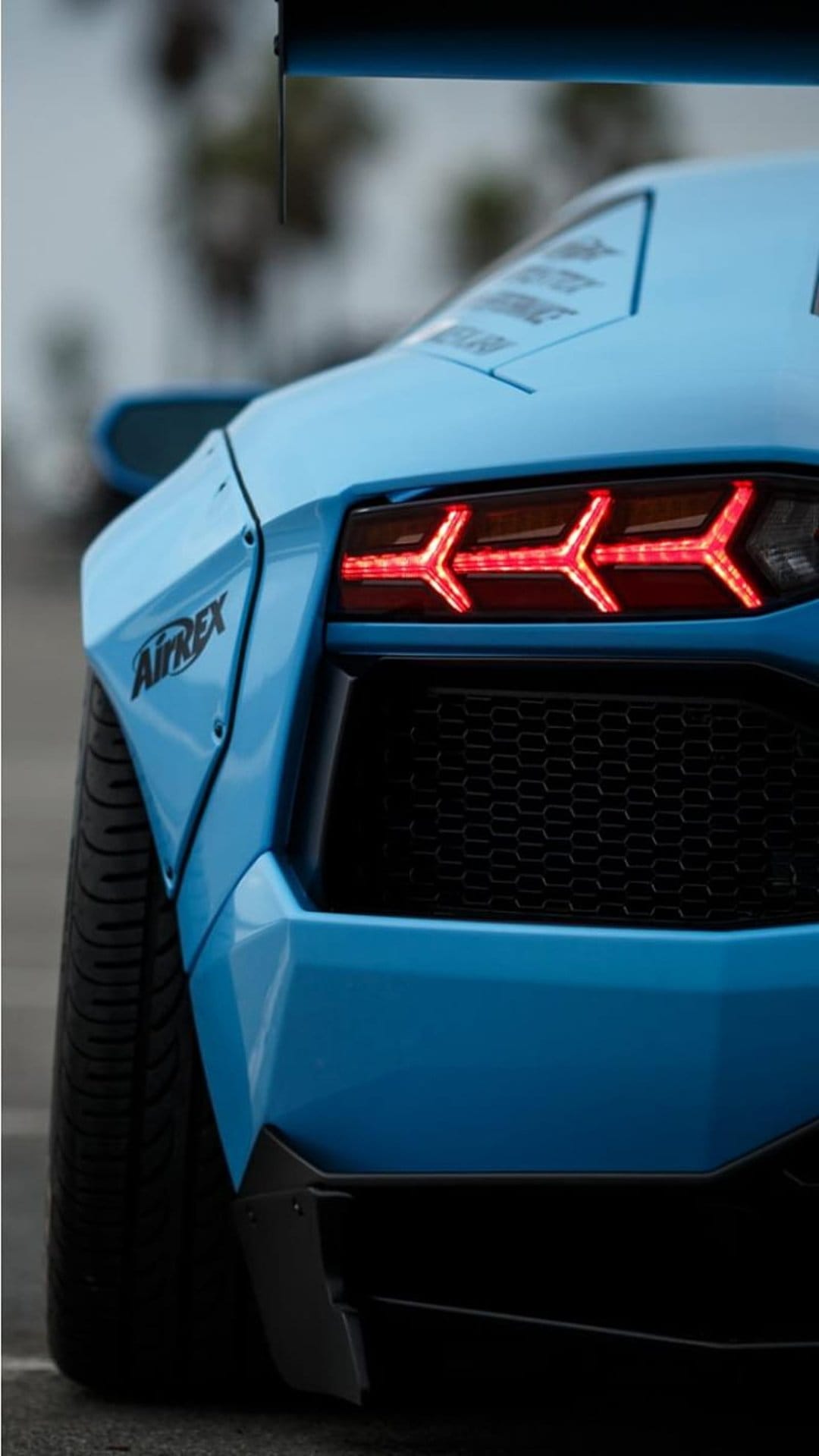 Blue Lamborghini Aventador rear shows red Y-shaped LED taillights, a large black wing, and widebody fenders.