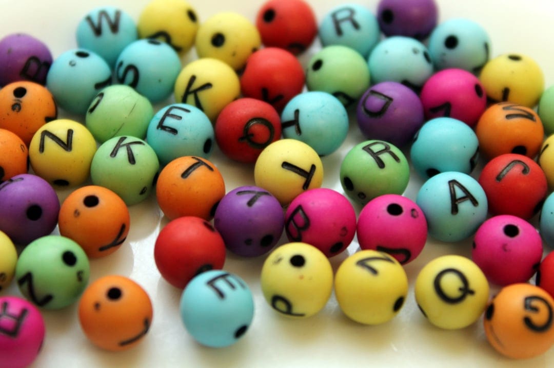 Multi-colored round alphabet beads with black letters are scattered in a bright, macro close-up composition.