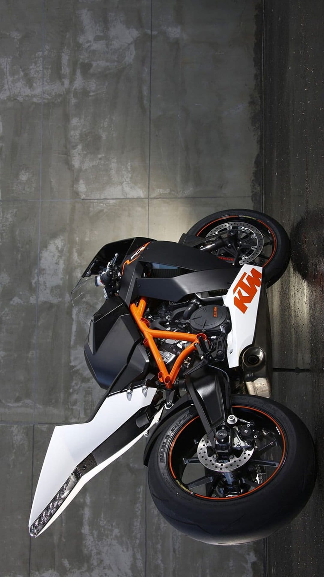 KTM Super Duke R motorbike featuring an orange frame and black accents parked beside a weathered concrete wall.