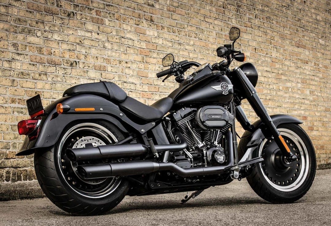Black Harley-Davidson motorcycle parked against a tan brick wall with solid silver rims and dual exhaust pipes.