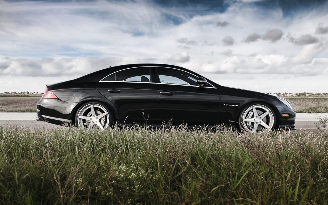Black Mercedes-Benz CLS sedan with silver wheels in tall grass under a cloudy sky for desktop background.