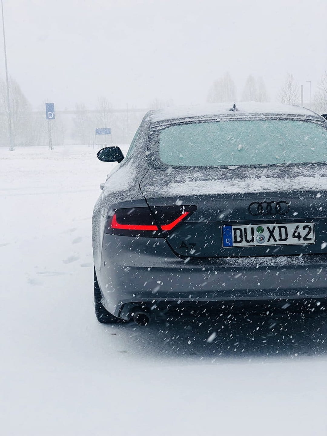 Audi A7 rear view with glowing red taillights and 'DU XD 42' license plate during a heavy winter snowfall at night.