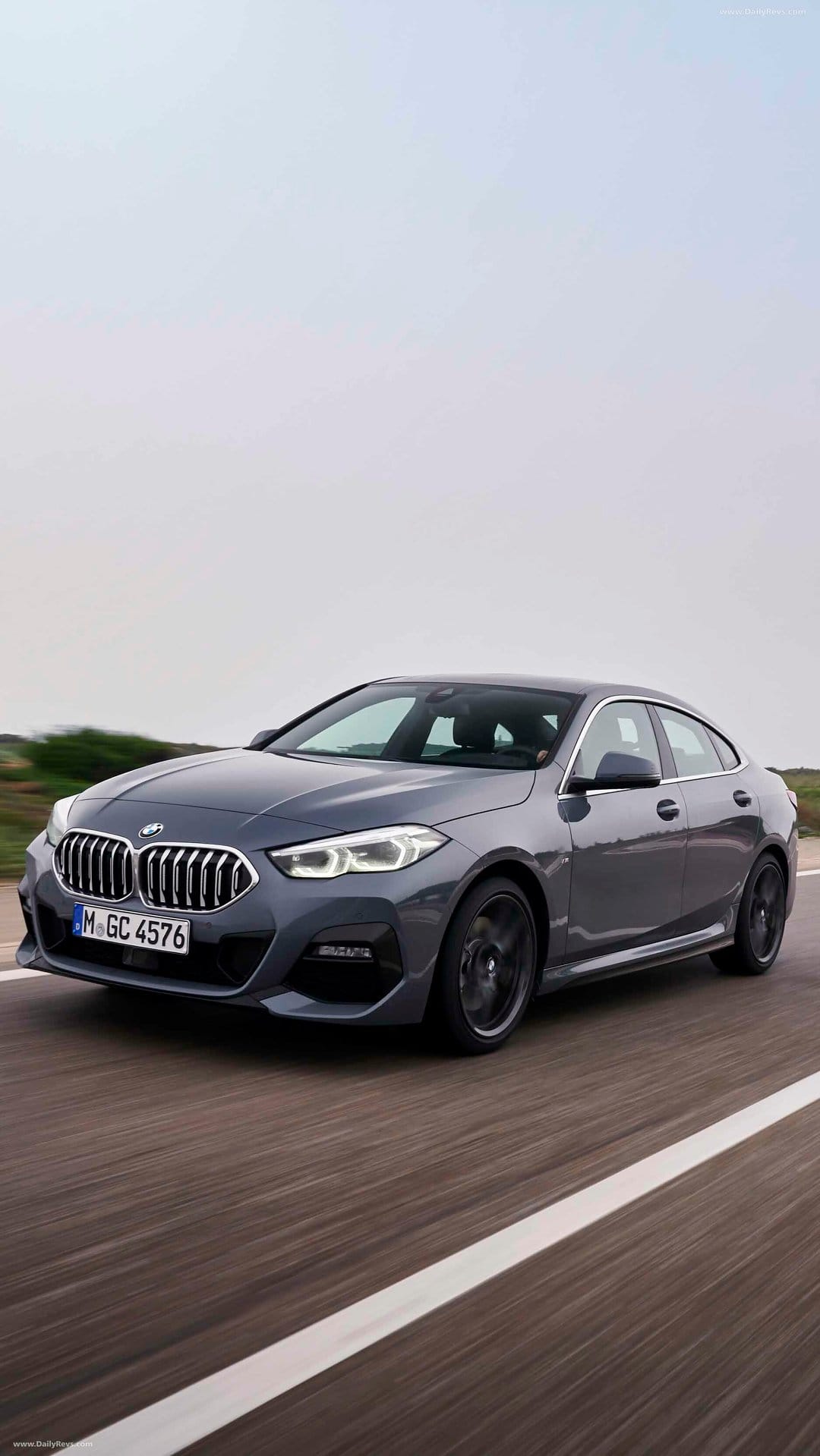Grey BMW Gran Coupe sedan driving on a highway with motion blurred wheels under a soft overcast sky.