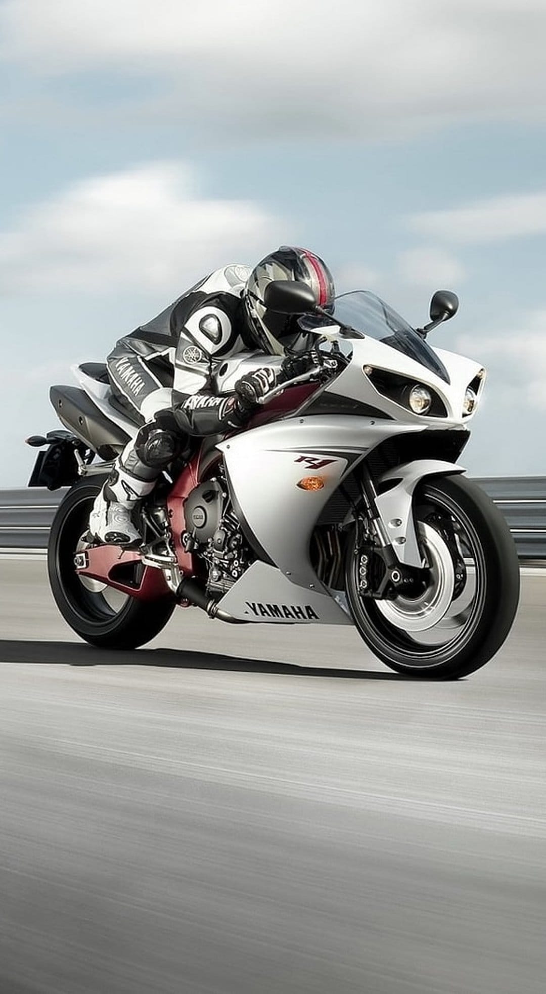 Racer on a white Yamaha R1 motorcycle leans into a track corner wearing professional gear and a full helmet.