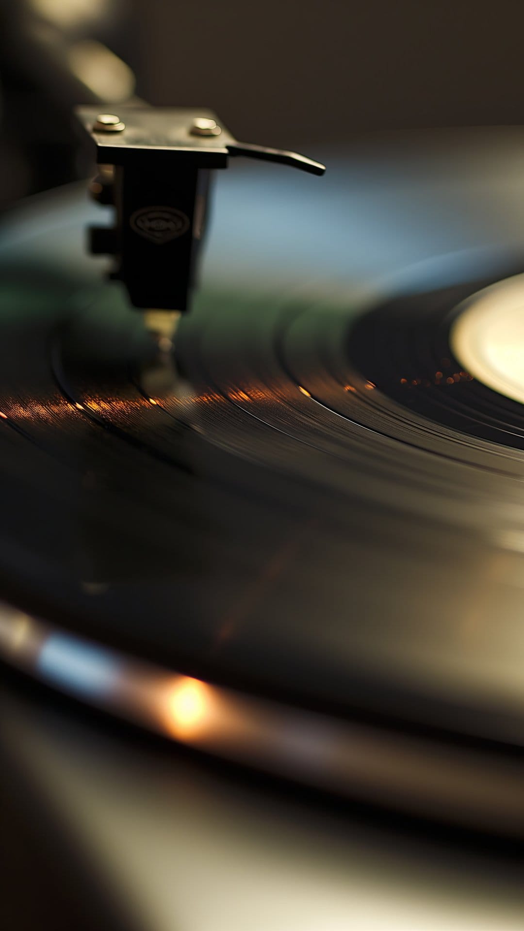 Metallic turntable stylus needle rests on the dark grooved surface of a spinning vintage vinyl record disc.