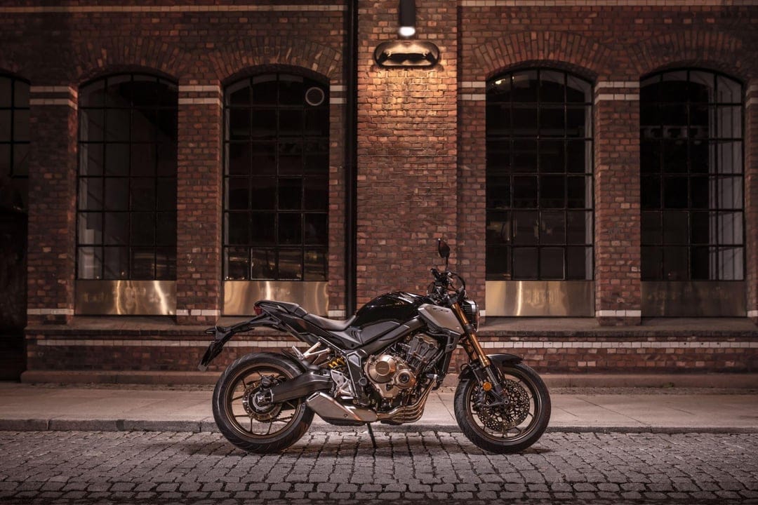 Side view of a black Honda motorcycle on a cobblestone street in front of a lit red brick wall at night.