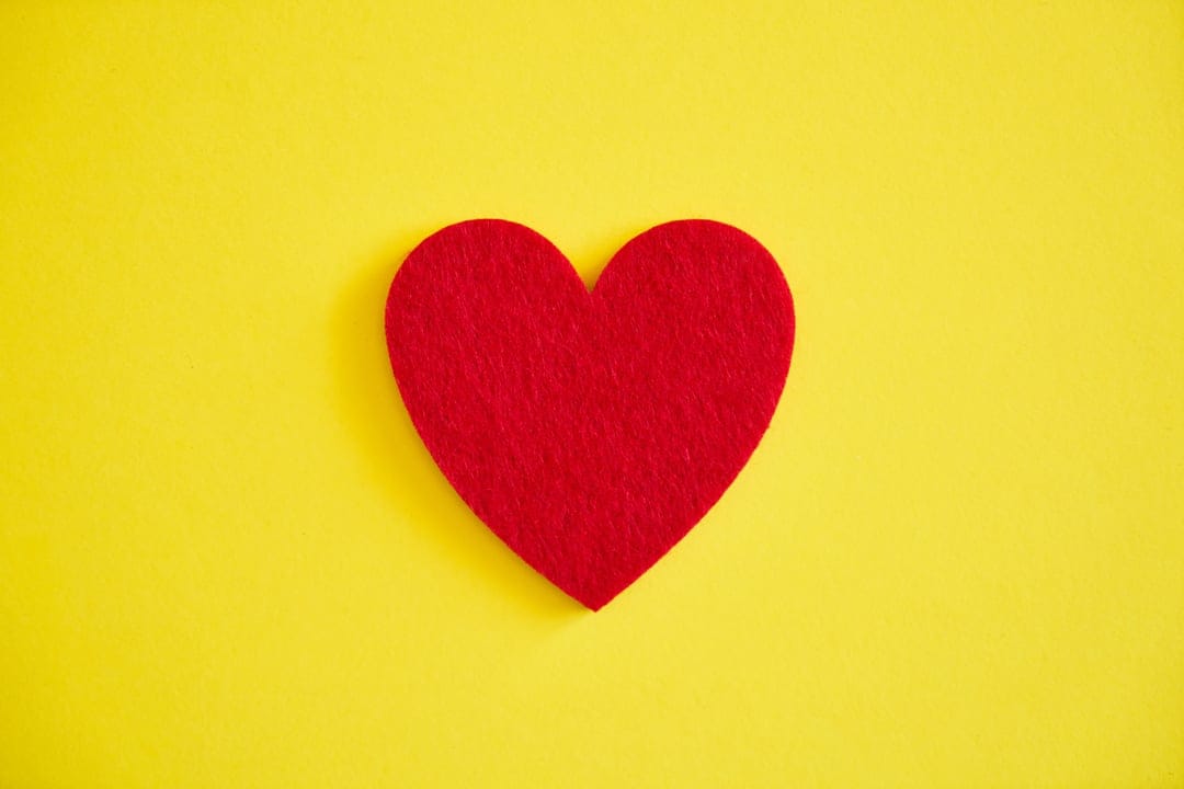 Red heart symbol centered on a solid bright yellow background with sharp edges and vivid color saturation.