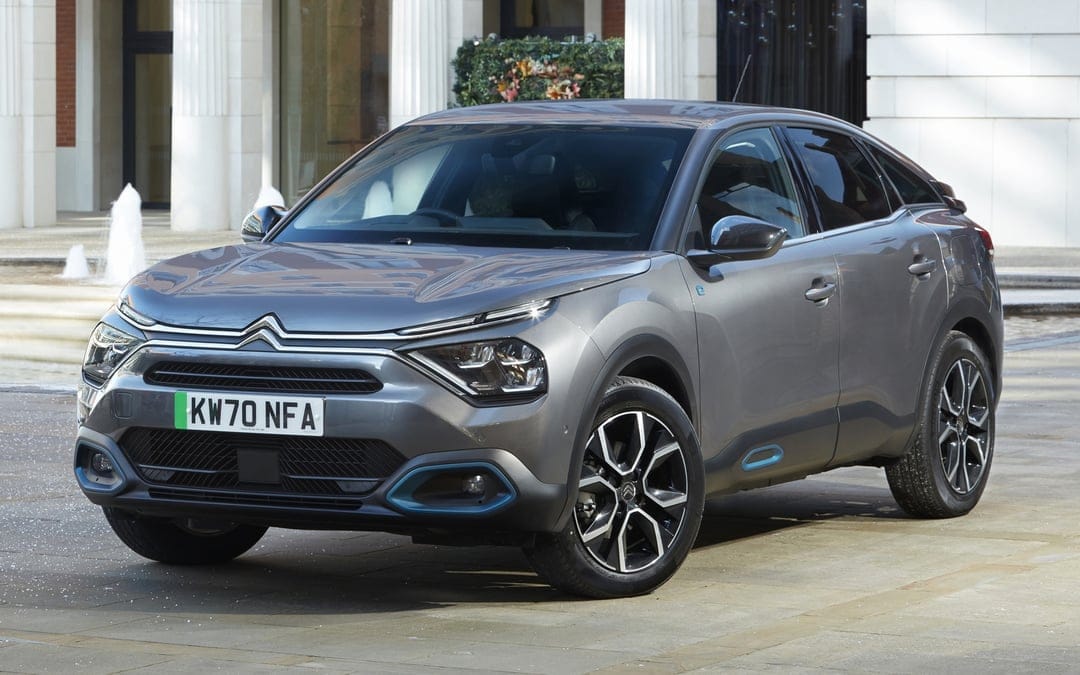 Grey Citroën e-C4 electric car parked on a stone plaza in front of white columns and small water fountains.