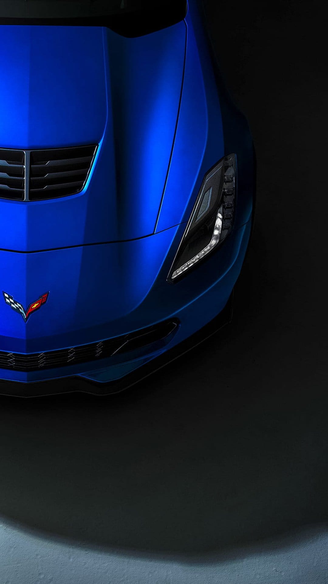 Blue Corvette C7 front hood and grille featuring the silver crossed flags emblem with modern LED headlights.