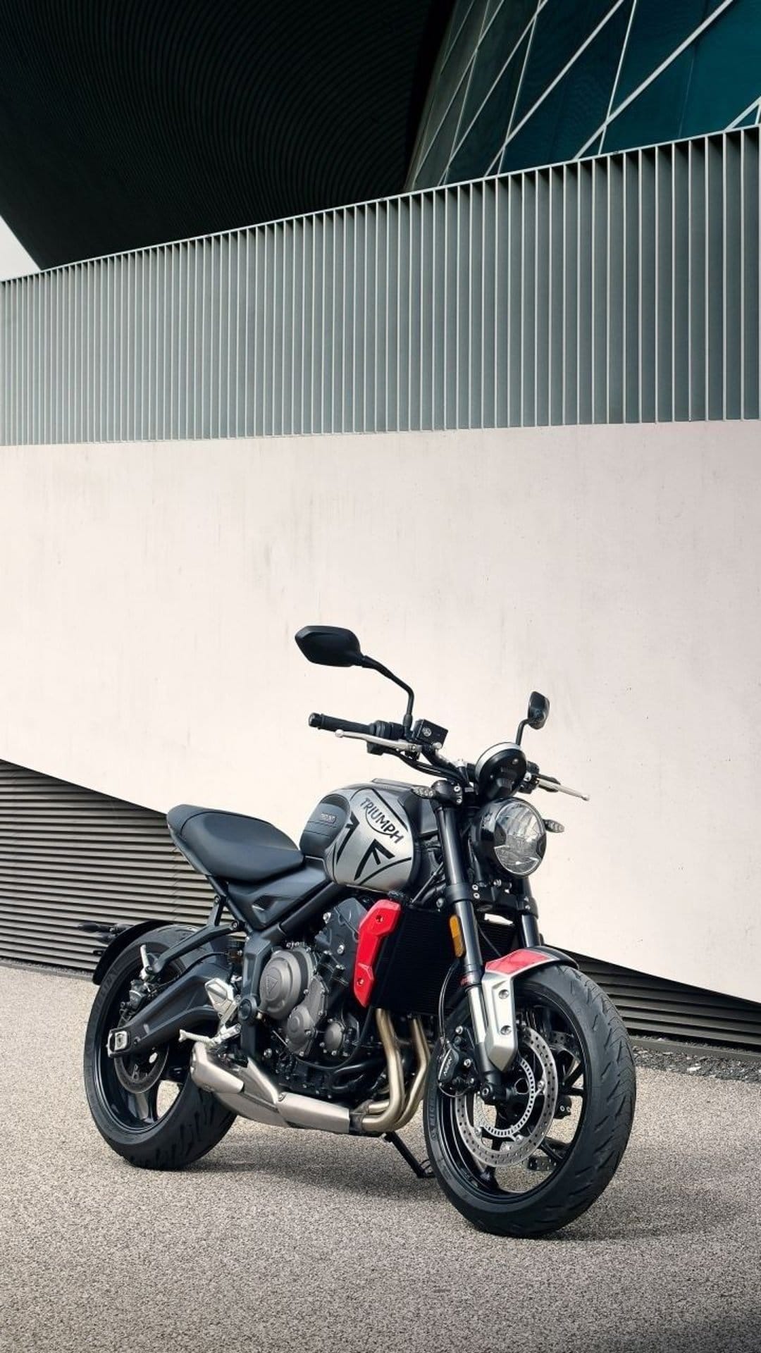 Triumph Trident motorcycle with a silver fuel tank parked on pavement in front of a curved modern building facade.