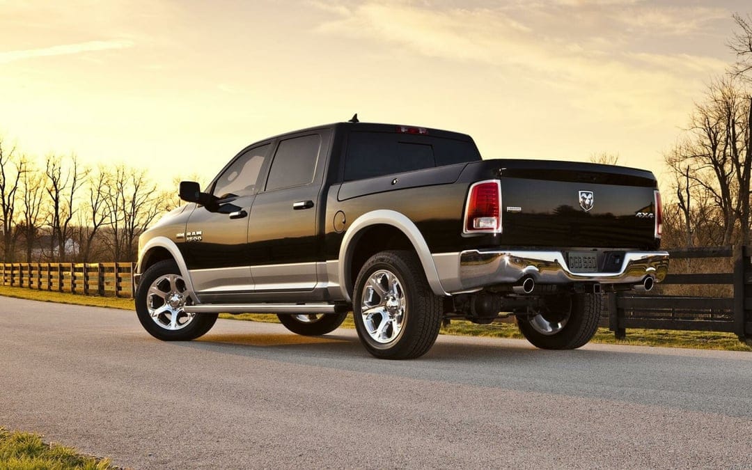 Black Ram 1500 Laramie truck with chrome rims on a country road during a golden sunset with rural scenery.