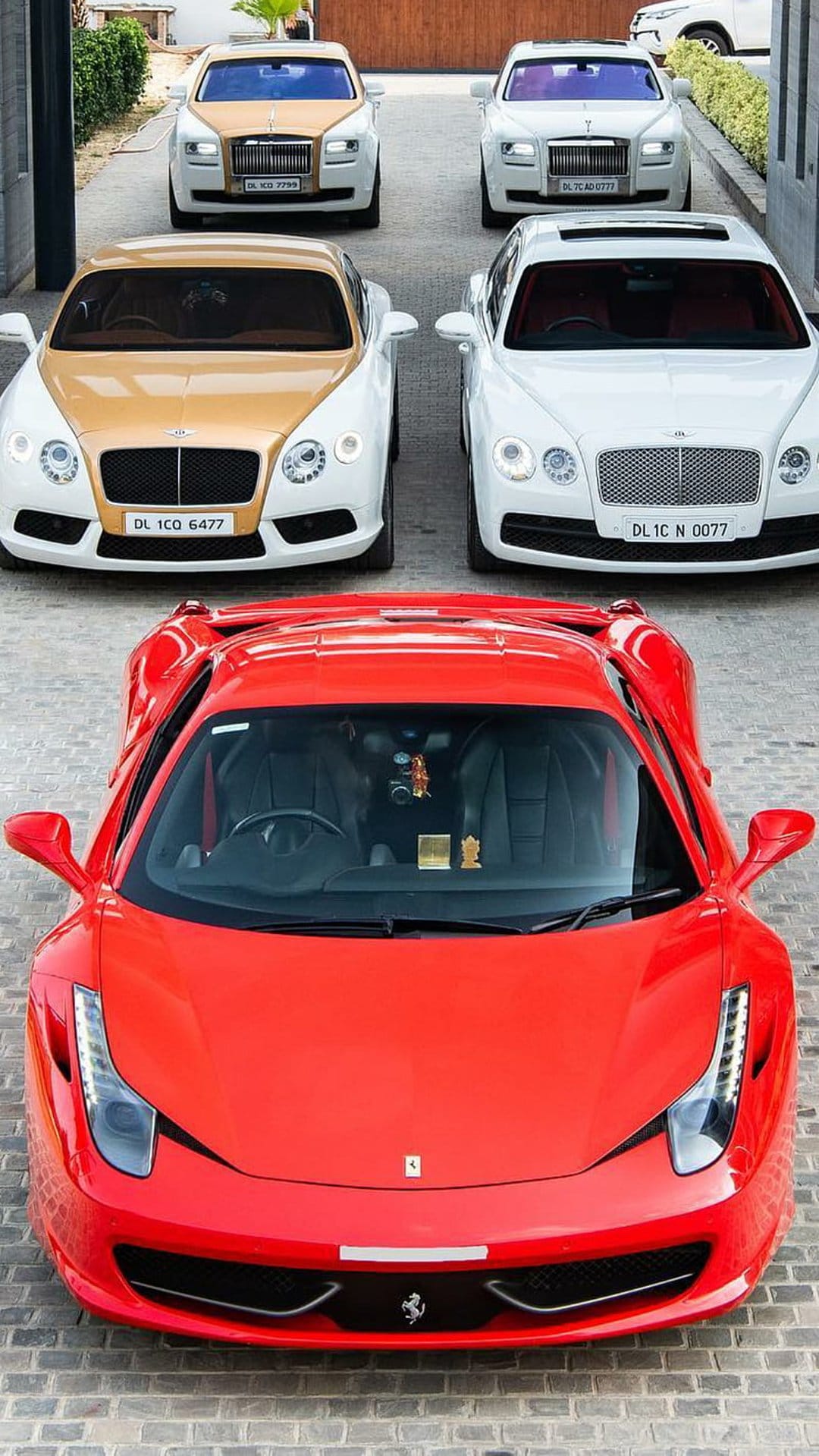 Vibrant red Ferrari sits before white Rolls-Royce and Bentley cars in a high-end luxury vehicle showroom.