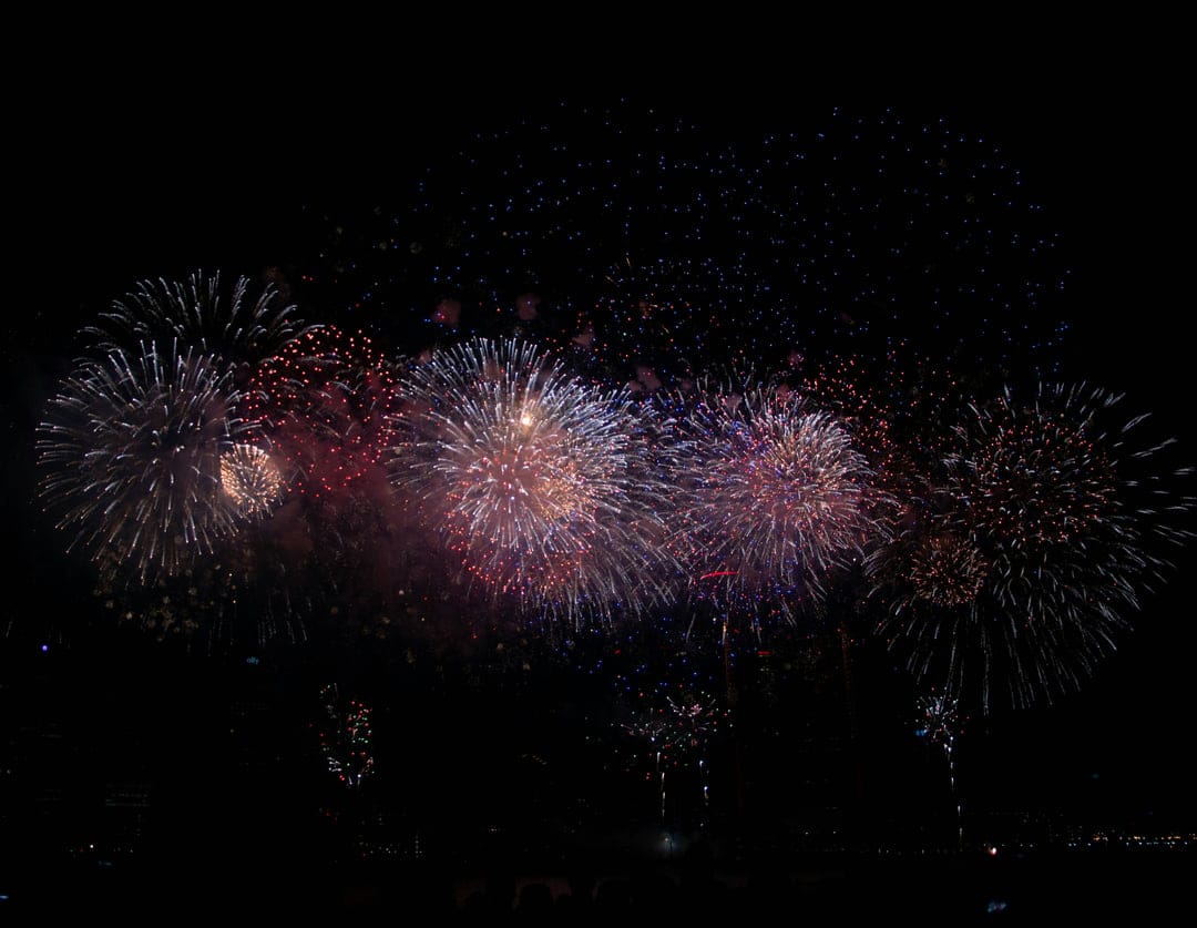 Crimson and blue fireworks exploding with shimmering light trails against a dark night sky in vertical orientation.