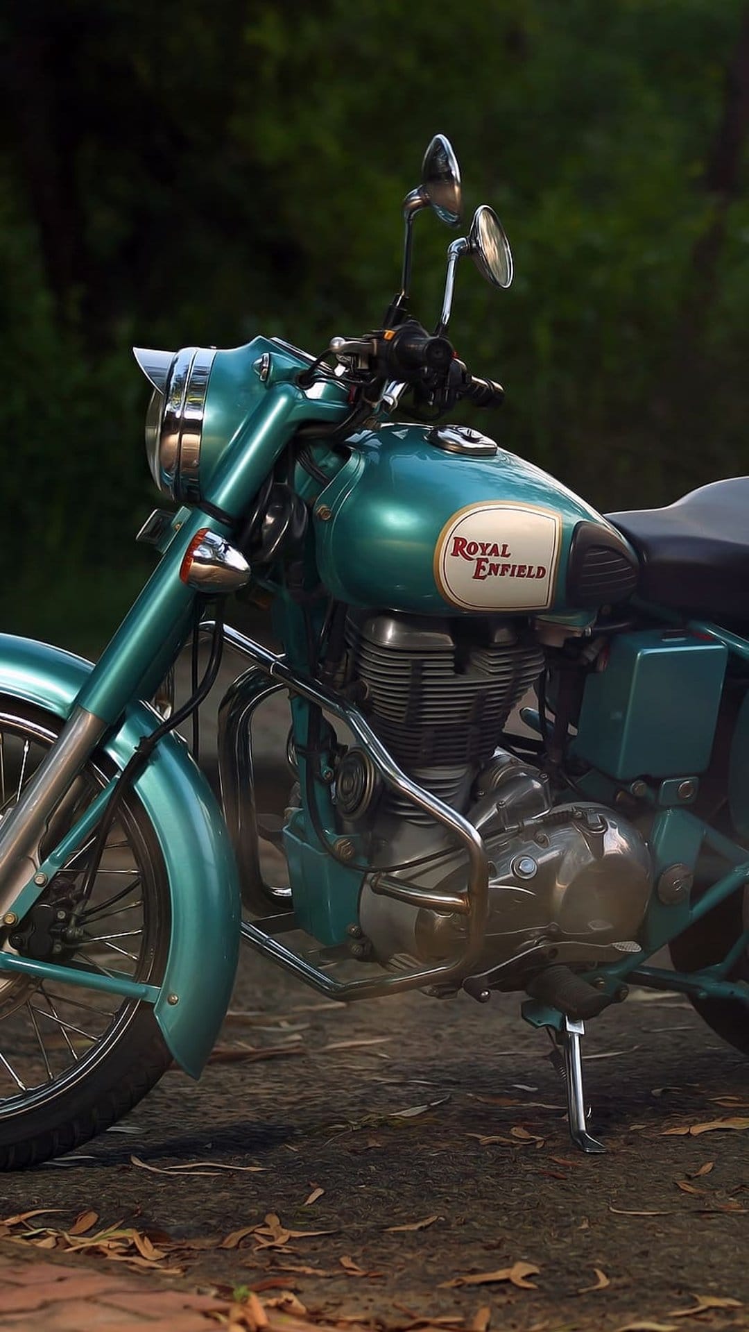 Teal Royal Enfield motorcycle showing a chrome engine and fuel tank logo on a path with scattered brown leaves.