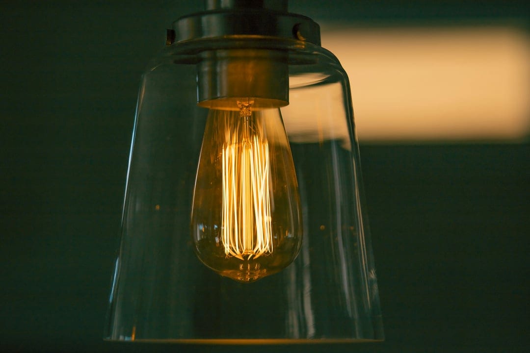 Edison light bulb with a glowing orange filament inside a clear glass pendant lamp casting warm amber light.