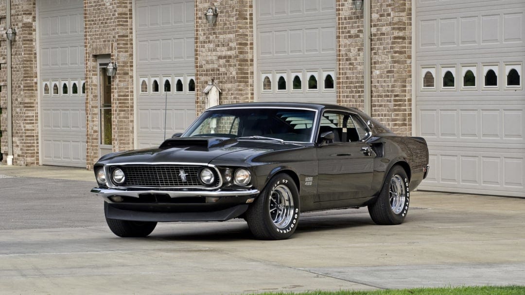Black 1969 Ford Mustang Boss 429 parked in front of brick garage doors under natural daylight.