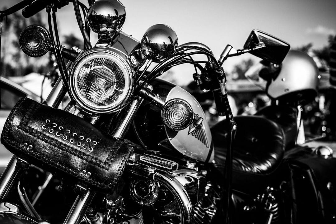 Close-up of a classic motorcycle headlight and leather tool bag in high-contrast black and white lighting.