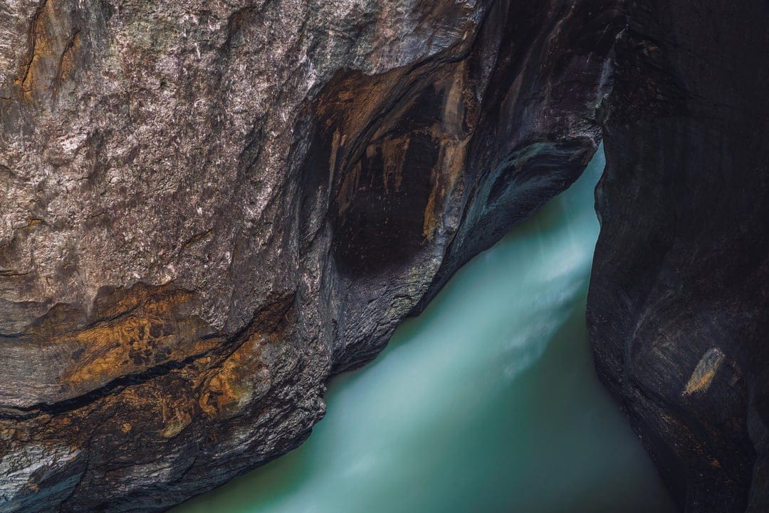 Turquoise water winds between steep, dark rock walls in a narrow gorge with smooth long-exposure motion effects.