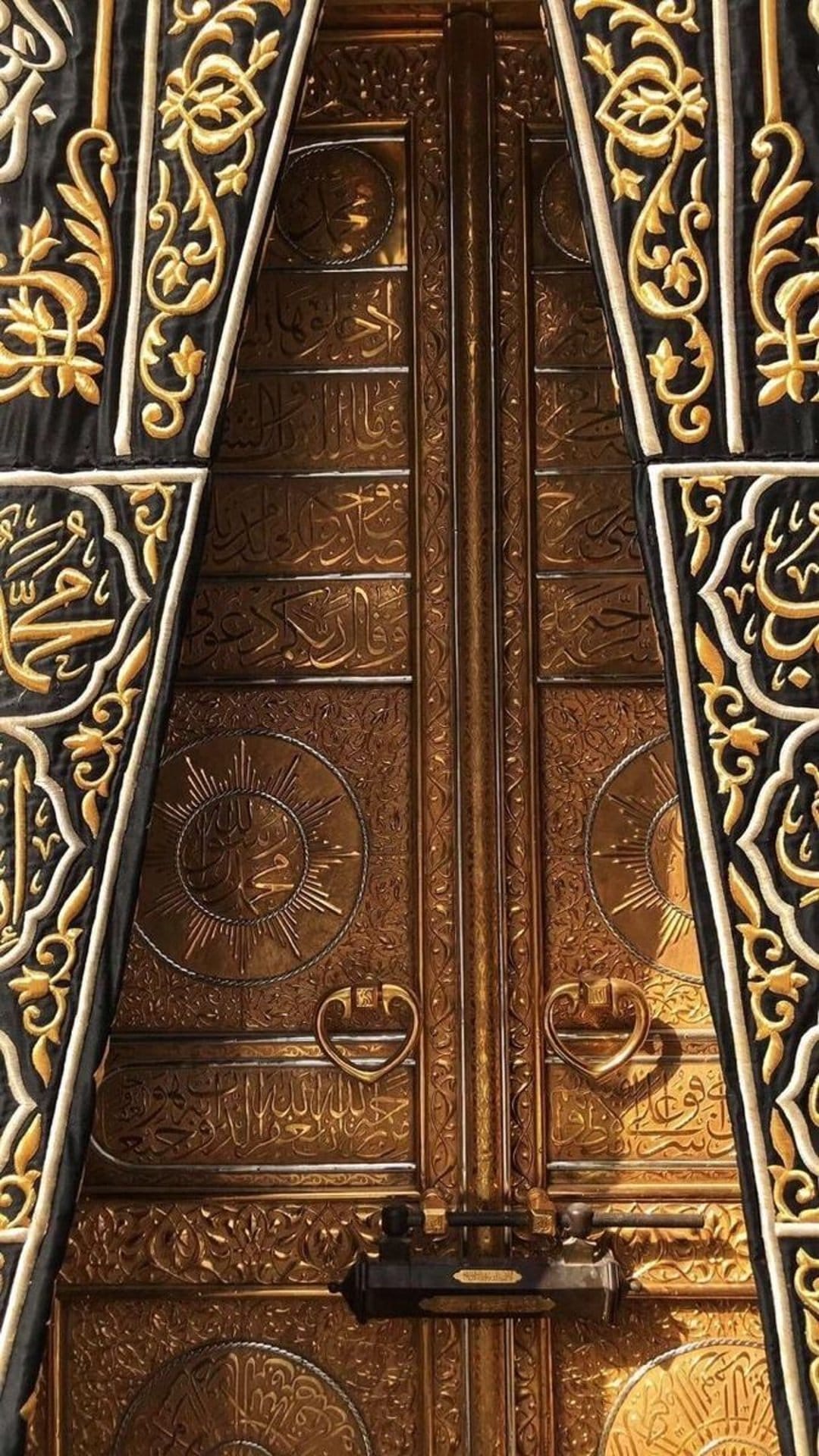 Golden Kaaba door featuring embossed Arabic calligraphy and floral patterns set against black silk drapery.