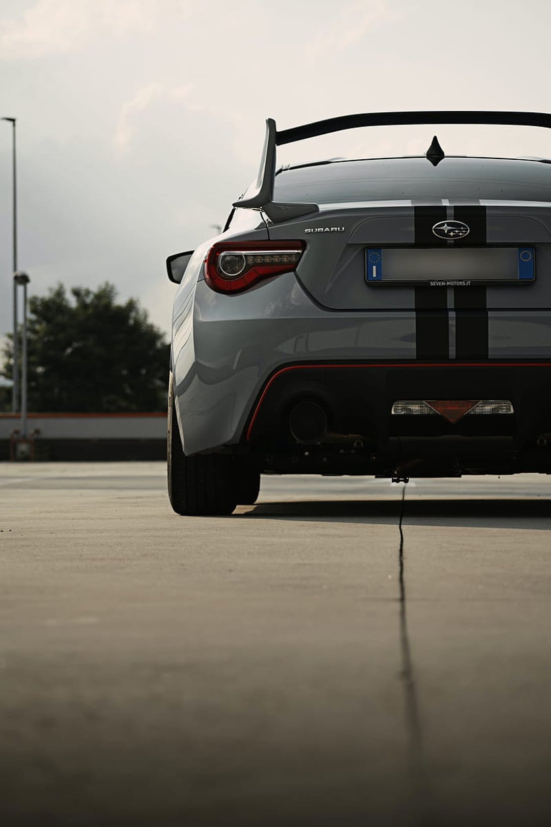 Subaru BRZ rear profile featuring black racing stripes, a large spoiler, and red accents on a concrete ground.