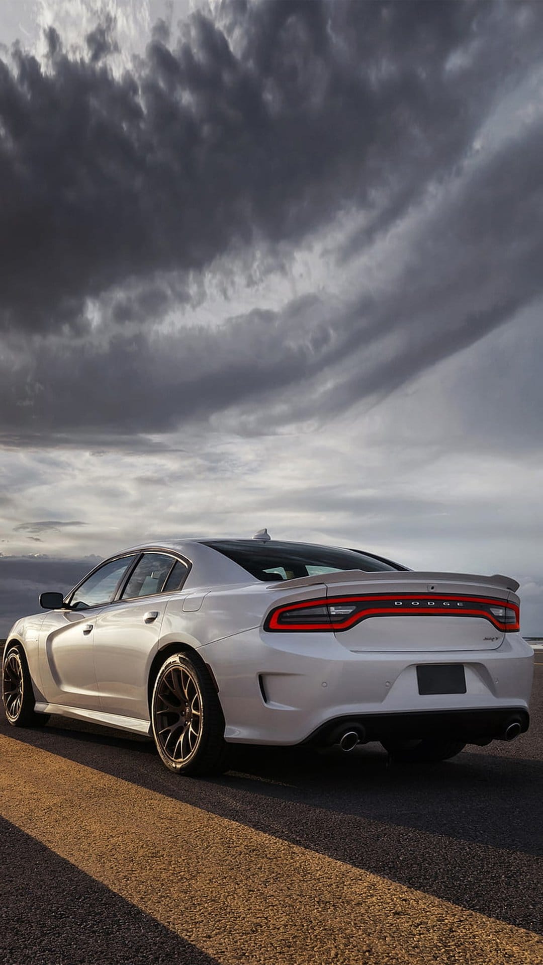 White Dodge Charger SRT Hellcat rear view on asphalt under dark storm clouds with glowing red taillights.