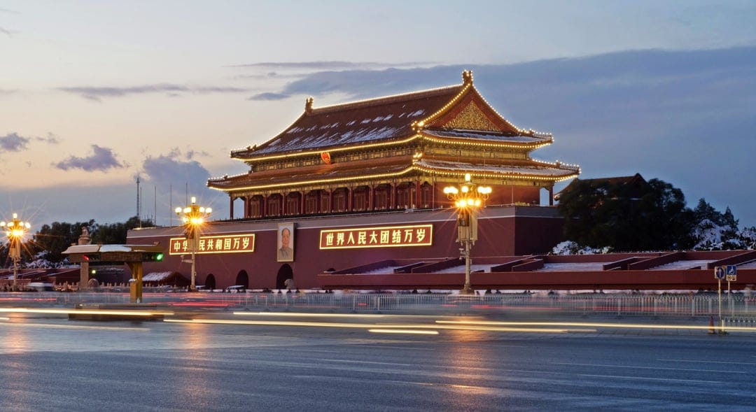 Tiananmen Gate illuminated at dusk with long exposure light trails from traffic on a Beijing city road.