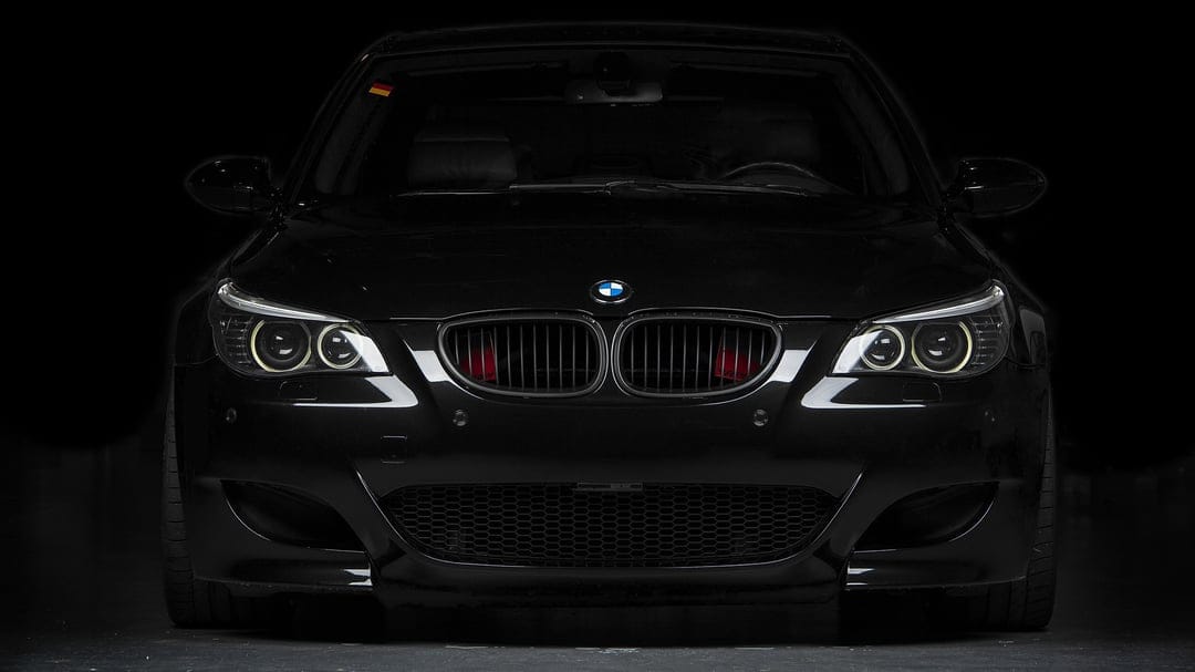 Front view of a black BMW M5 E60 with yellow halo headlights and red air scoops in the kidney grille.