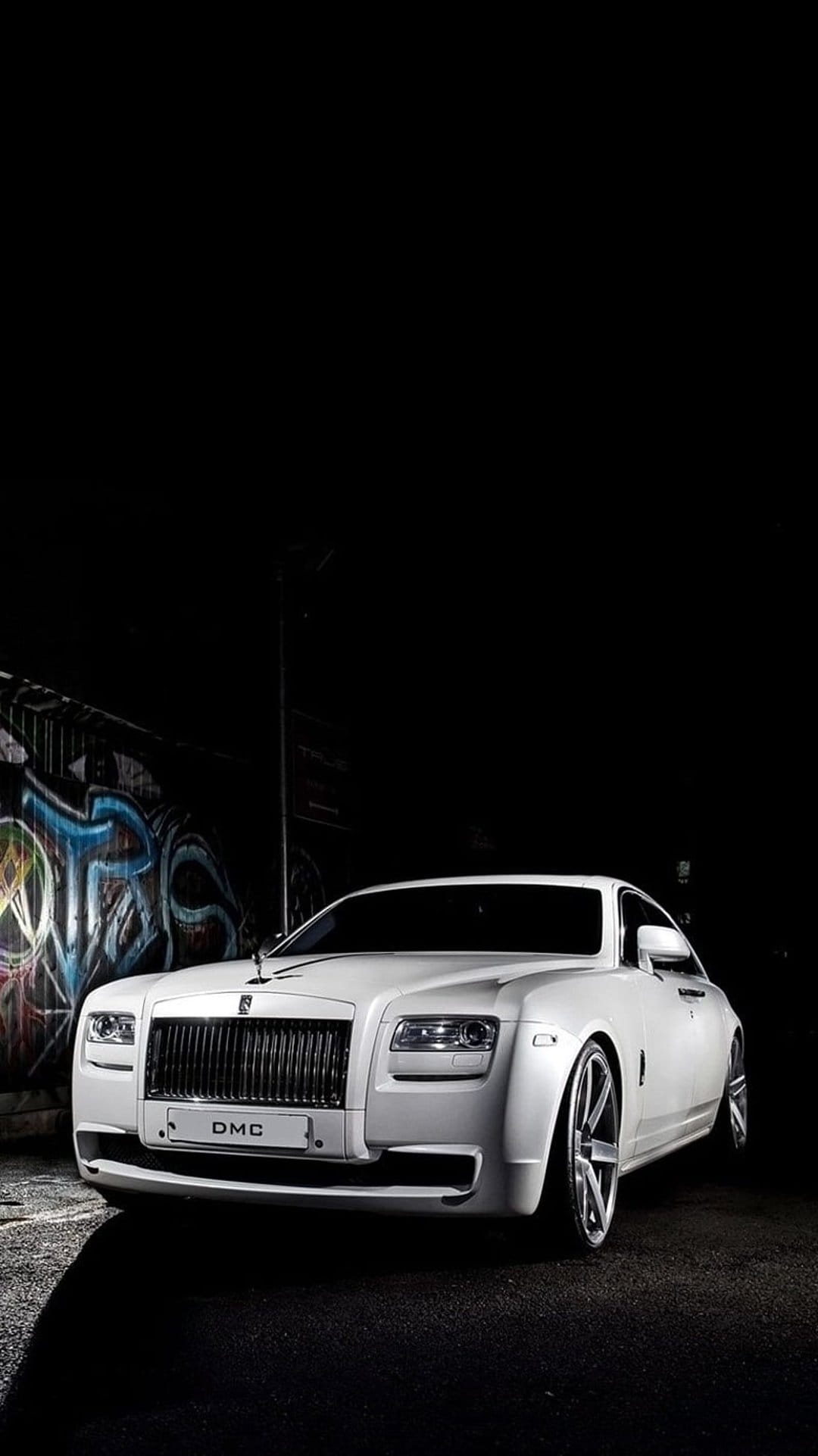 Rolls-Royce Ghost DMC luxury sedan positioned against a vibrant spray-painted urban wall with dramatic lighting.