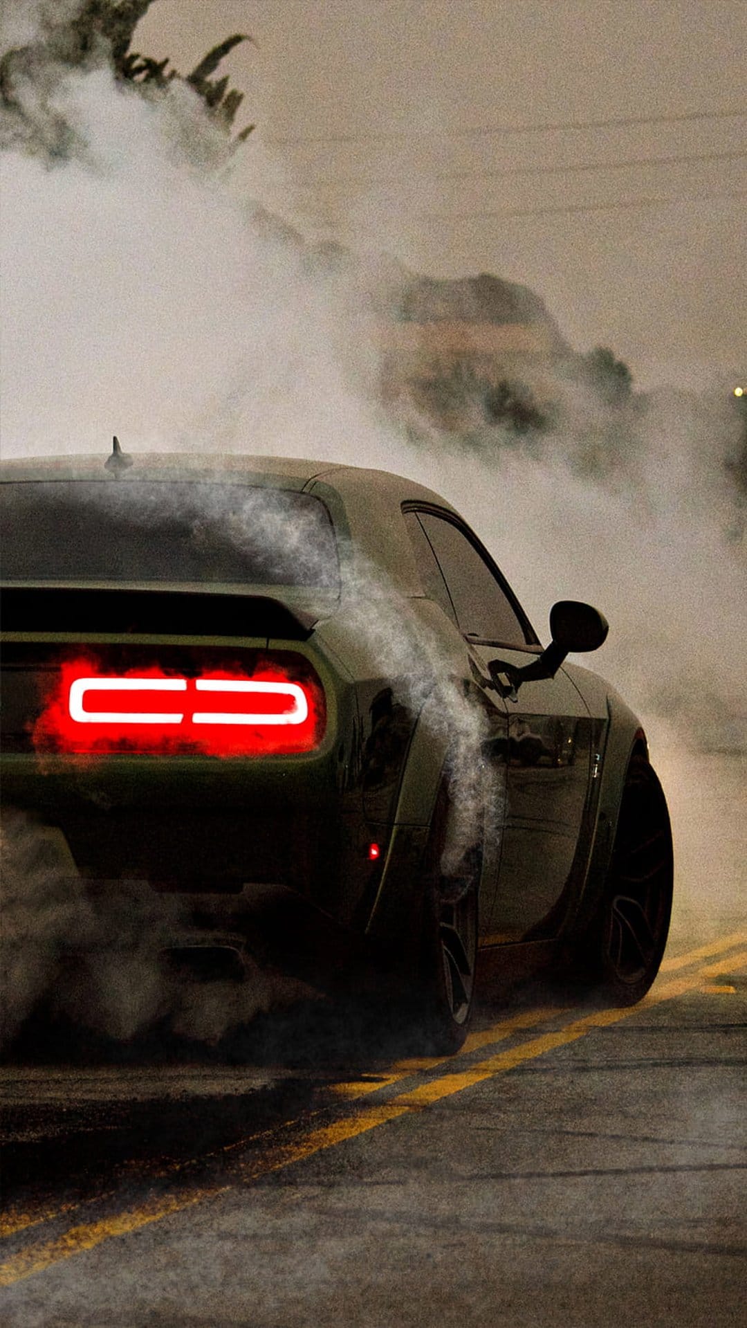 Dark green muscle car drifting on asphalt with thick white smoke and glowing red taillights in a night scene.