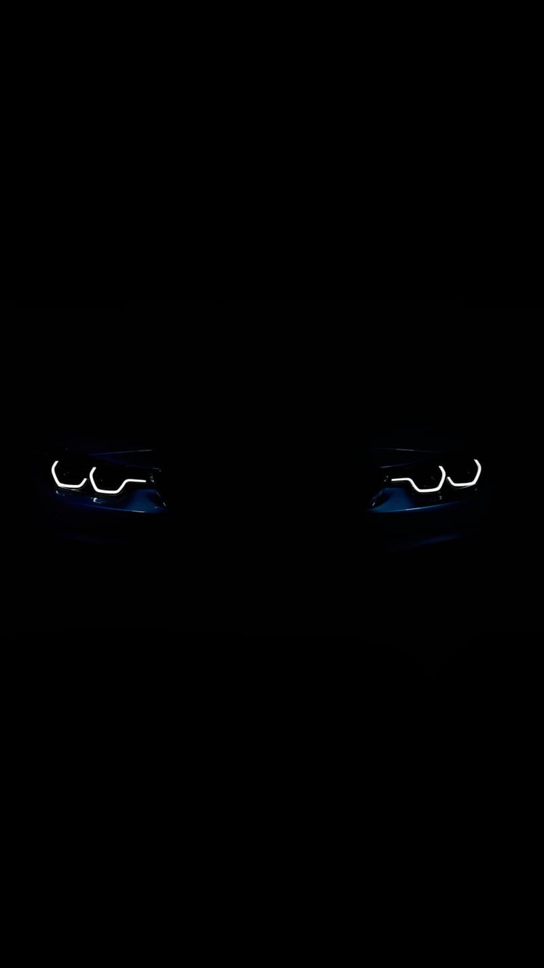 Blue car headlights glowing in the dark, highlighting the aerodynamic front end of a modern vehicle at night.