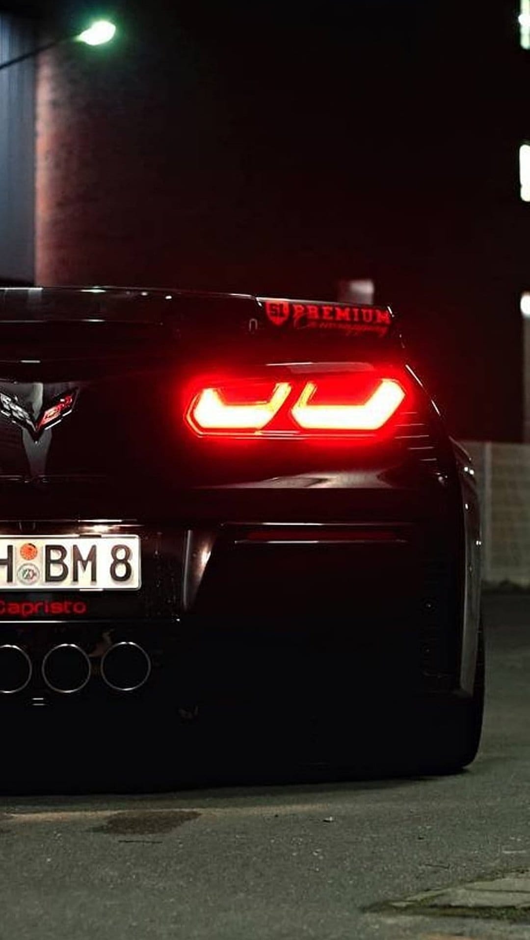 Black Corvette rear view displays glowing red taillights and quad exhausts against a dark brick street.