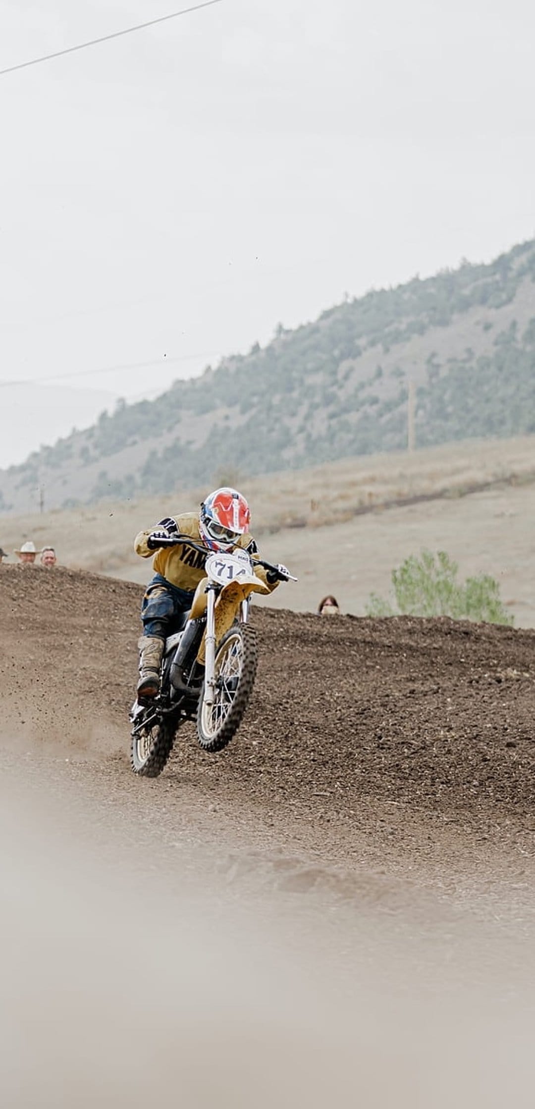 Motocross racer in a yellow jacket jumping a Yamaha motorcycle numbered 71 over a rugged dirt track slope.