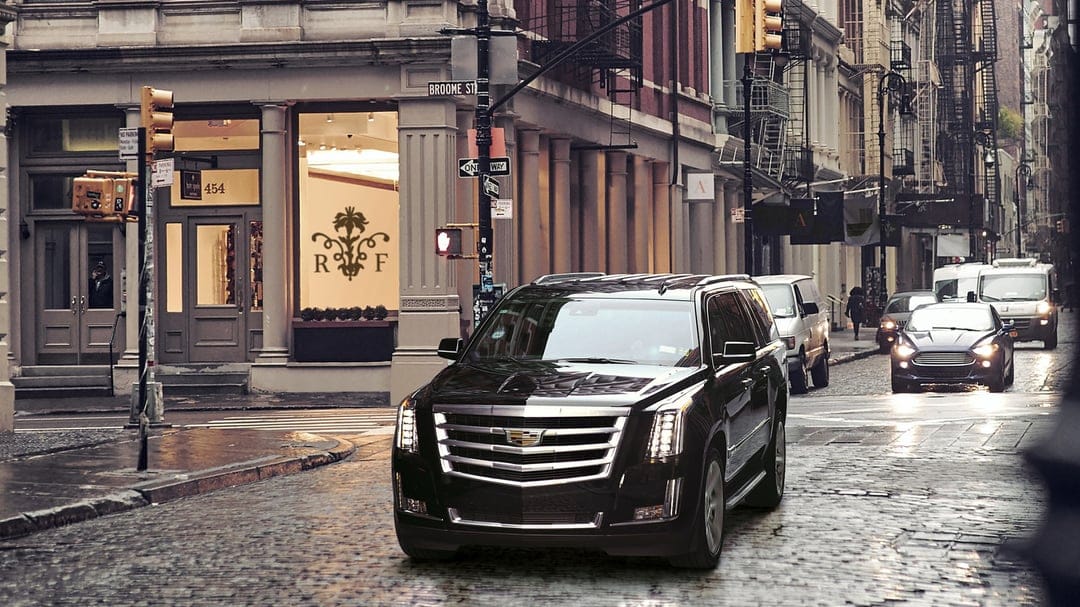 Black Cadillac Escalade parked on wet cobblestone Broome Street in NYC with historic buildings in the background.